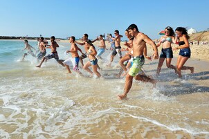 Un grupo de personas corriendo por una playa arenosa con olas rompiendo en la orilla.