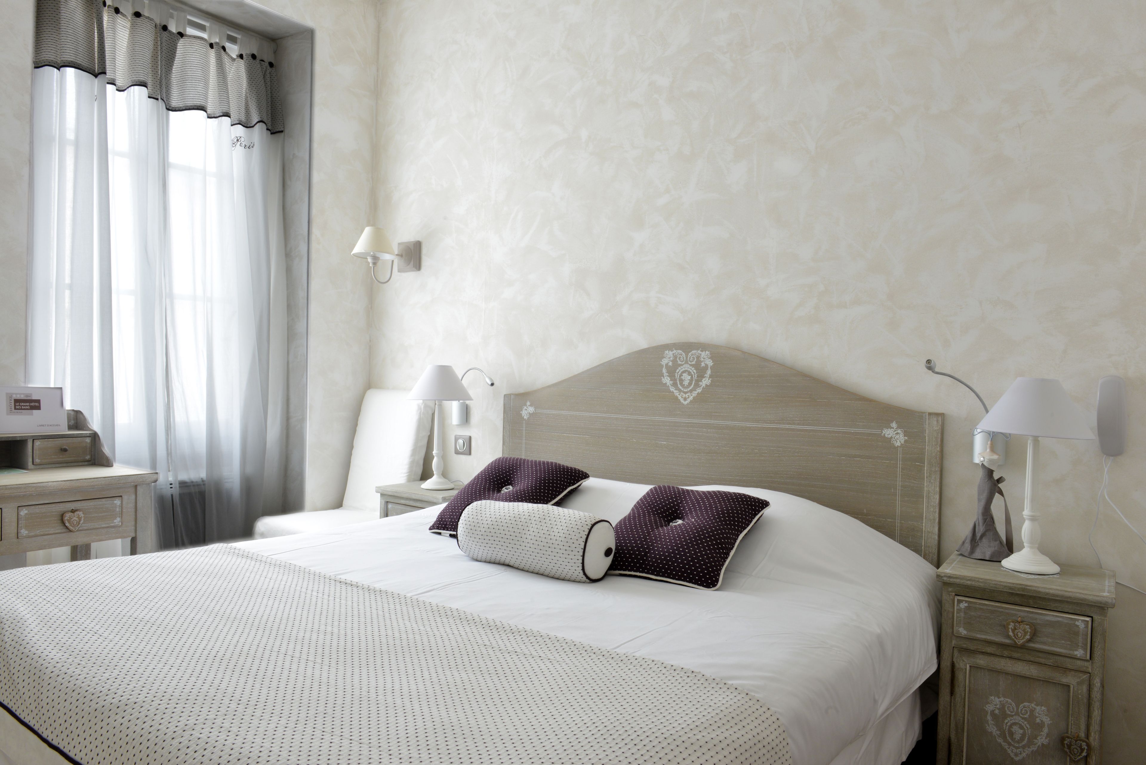 A neatly made bed with a heart-shaped headboard, two pillows, a bedside table with a lamp, and a nightstand with a lamp.