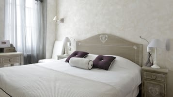 A neatly made bed with a heart-shaped headboard, two pillows, a bedside table with a lamp, and a nightstand with a lamp.