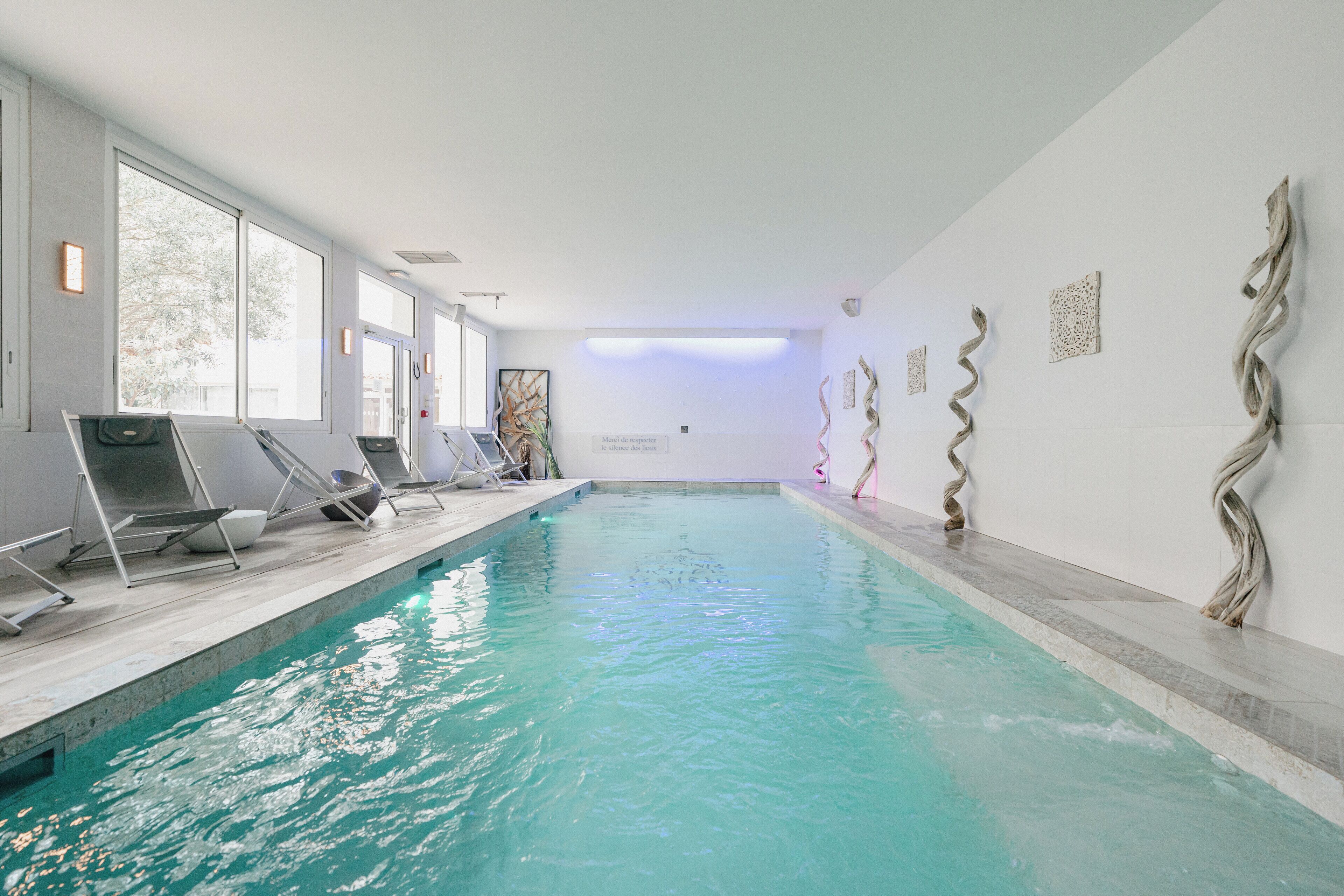 An indoor swimming pool with clear water, sun loungers, and artwork on the walls.