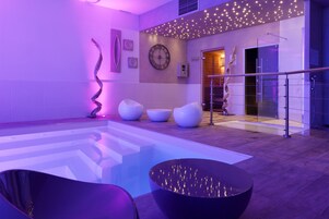 Un área de piscina interior moderna con un diseño geométrico en el suelo, un recipiente negro central y asientos contemporáneos.