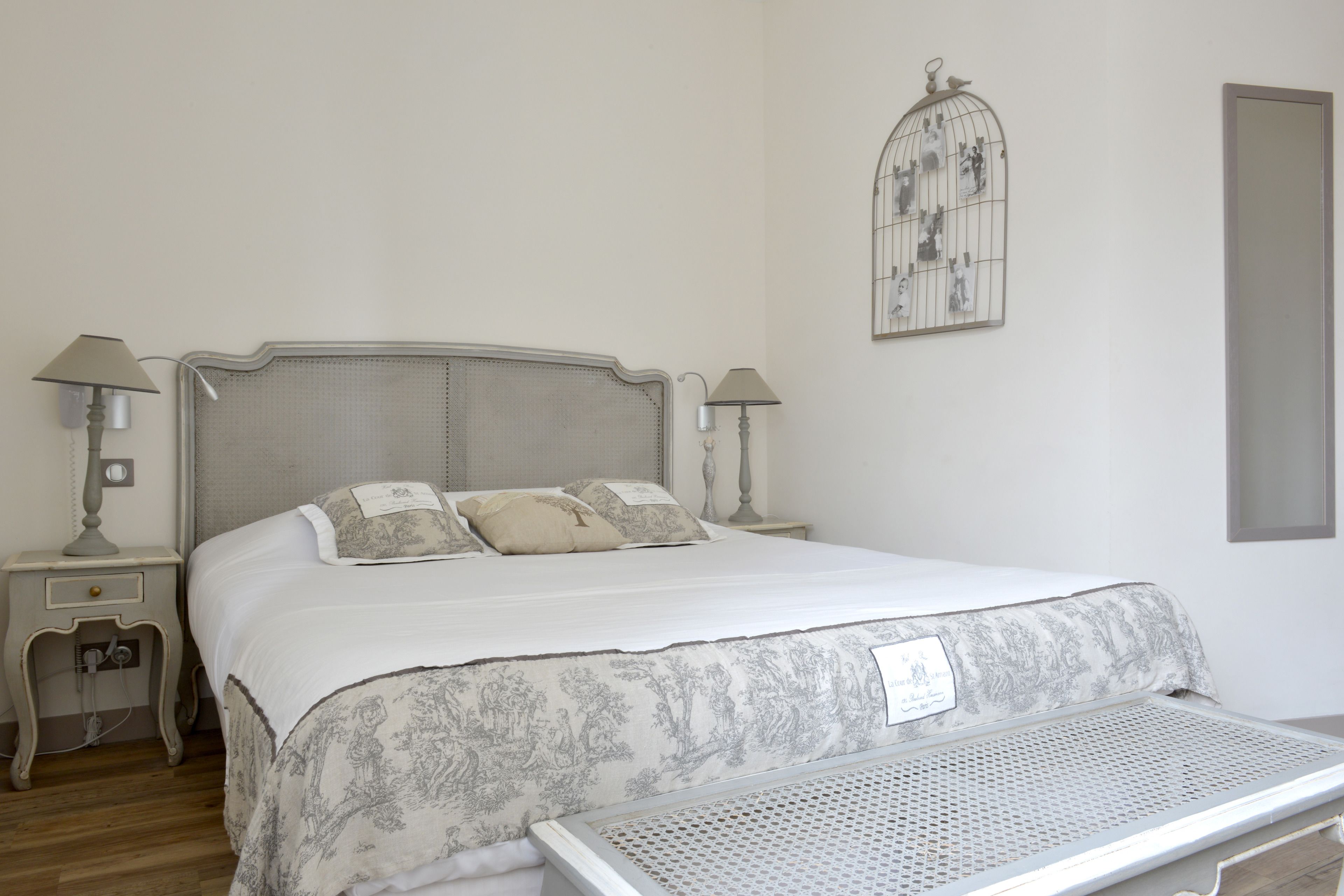 A neatly made bed with a headboard, two bedside tables with lamps, a decorative wall piece, and a large mirror.