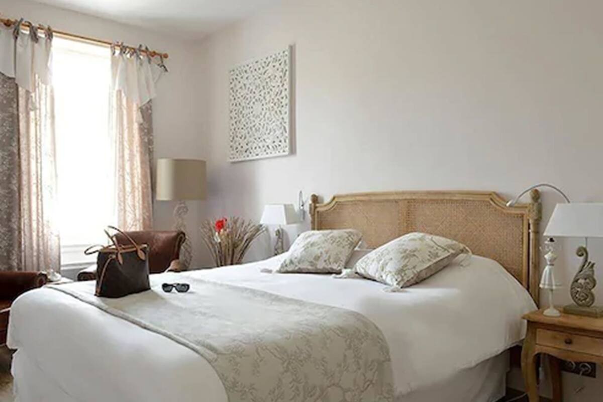 Un lit bien fait, avec une tête de lit, une table de chevet avec une lampe et une chaise sur laquelle est posé un sac à main.