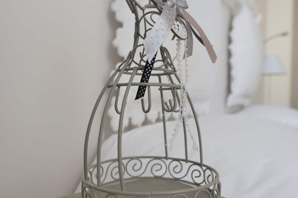 Une cage à oiseaux en métal contenant un objet décoratif, posée sur une table recouverte d’une nappe à motifs.
