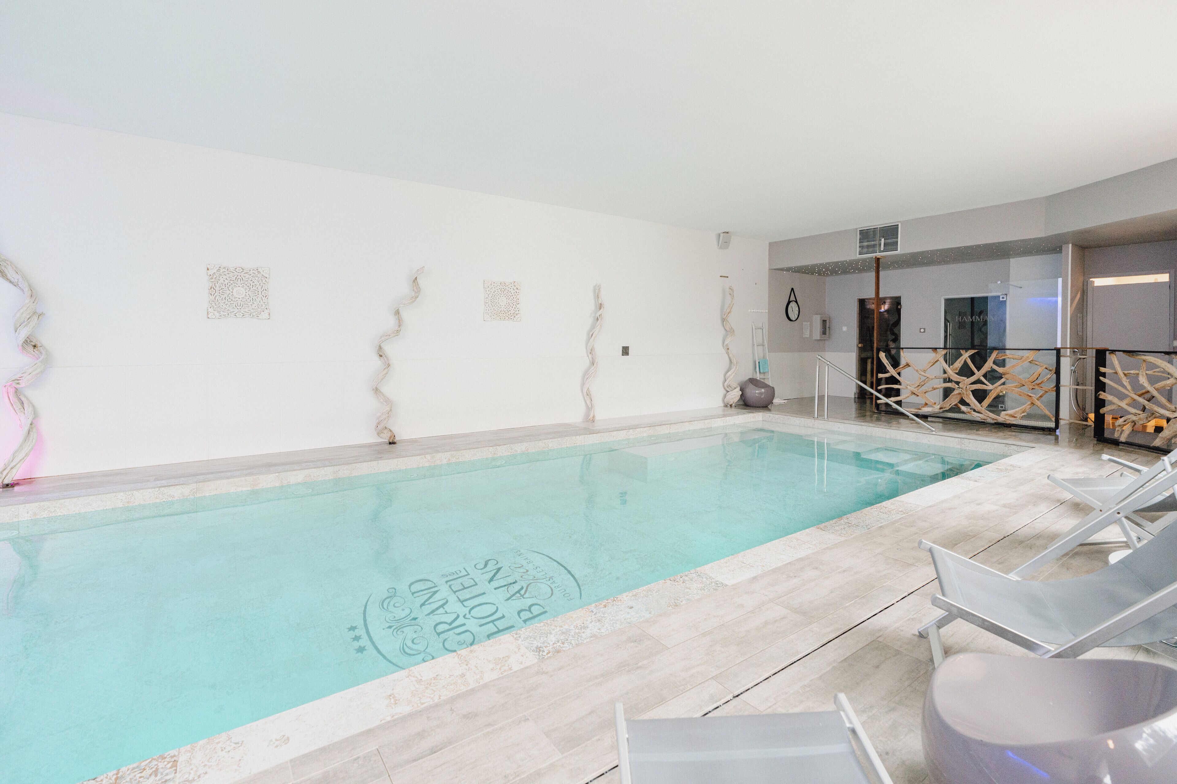 An indoor swimming pool with clear water, surrounded by lounge chairs and a wooden deck.