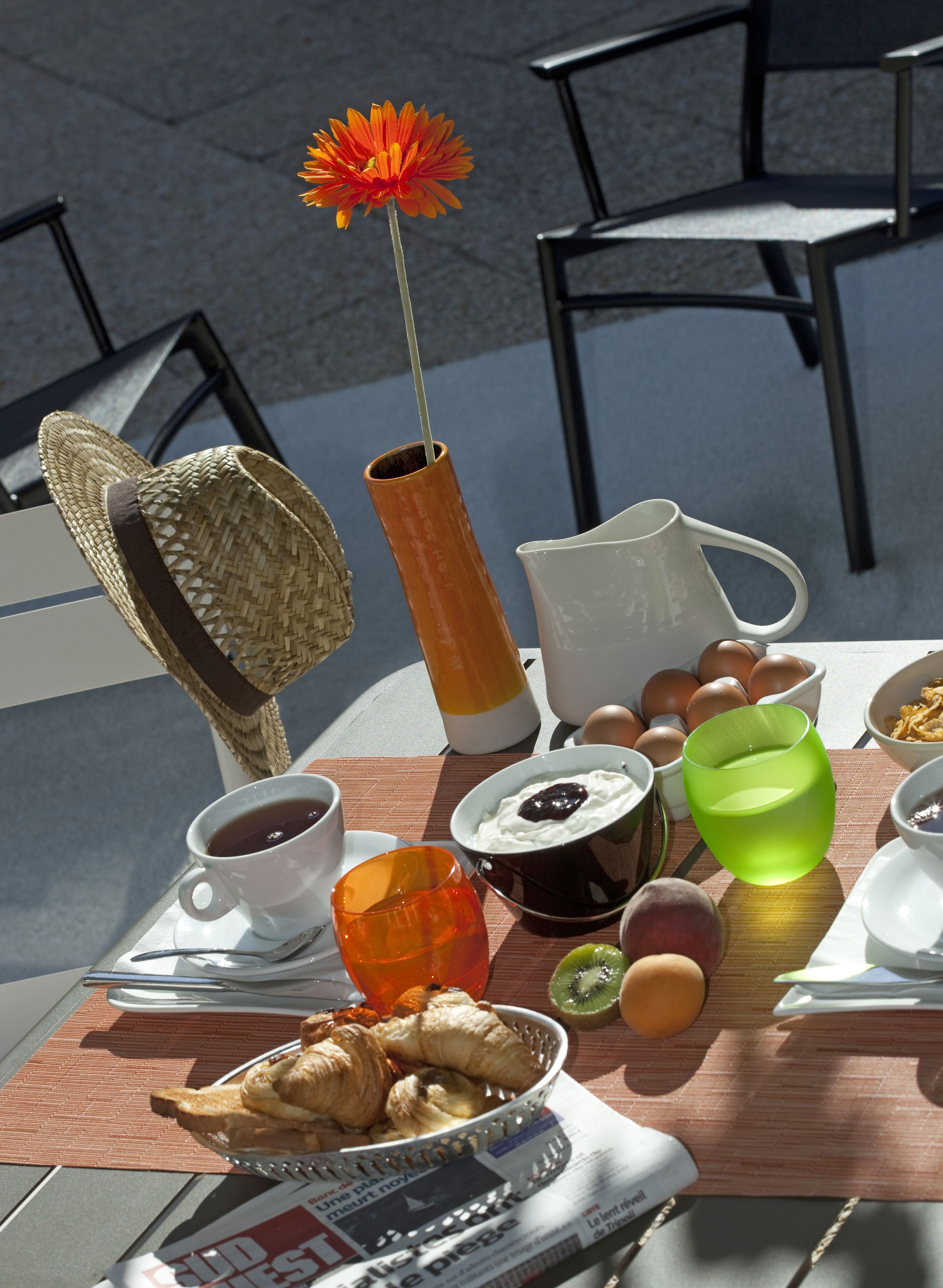 A breakfast table with croissants, eggs, a newspaper, and a vase with a flower.
