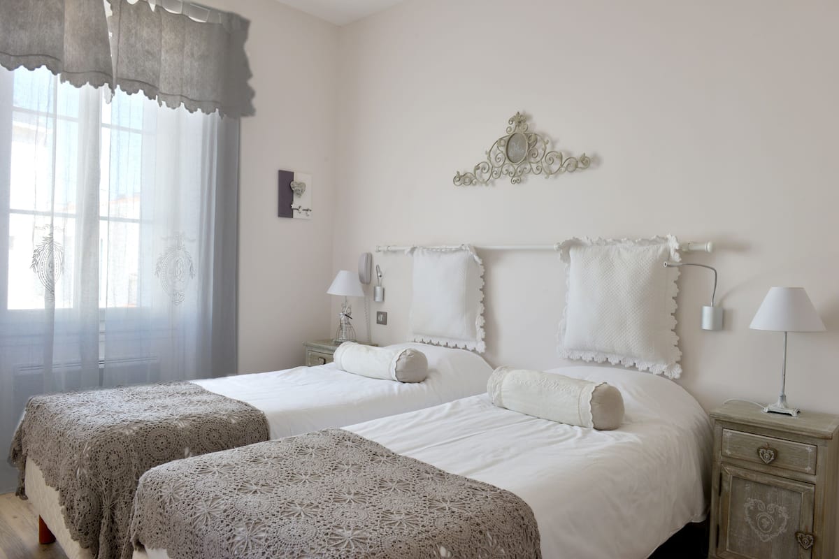 Une chambre avec deux lits, une fenêtre avec des rideaux légers, un élément décoratif mural et des lampes de chevet.