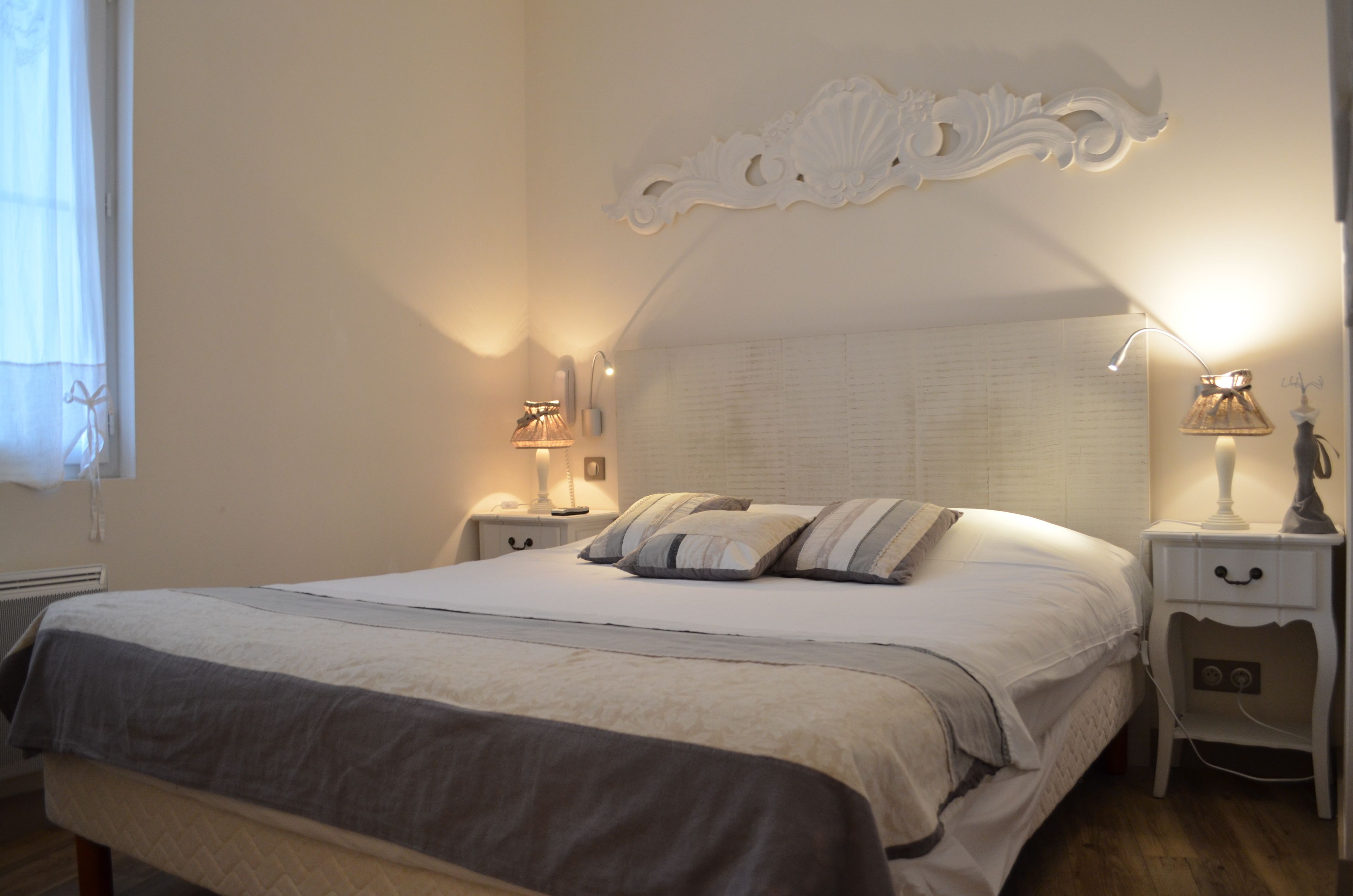A neatly made bed with a headboard, two bedside tables with lamps, and a window with curtains.