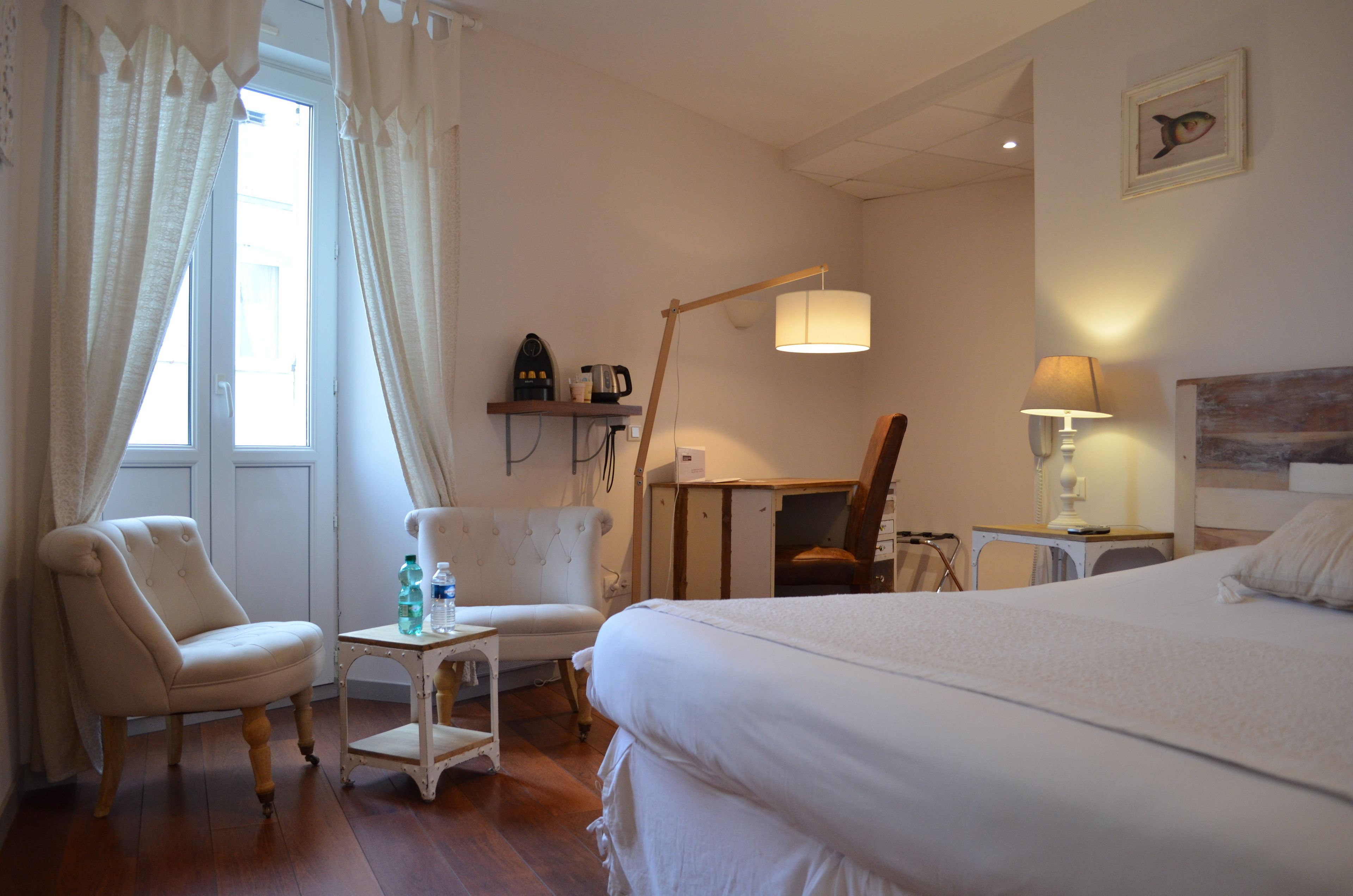 A hotel room with a bed, two chairs, a small table with a lamp, and a desk with a lamp.