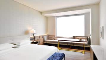 A hotel room with a large bed, a desk, a chair, and a window providing a view.