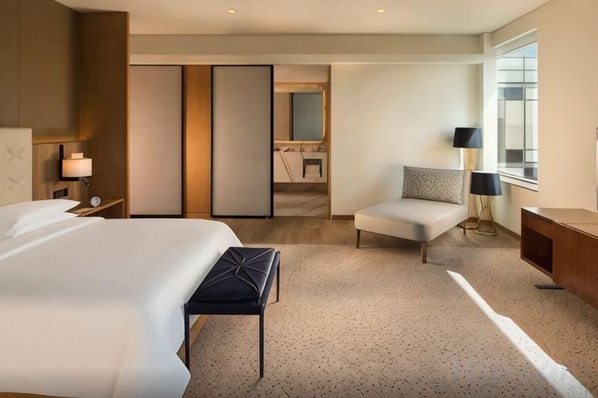 A hotel room with a large bed, a desk, a chair, a small table, and a window.