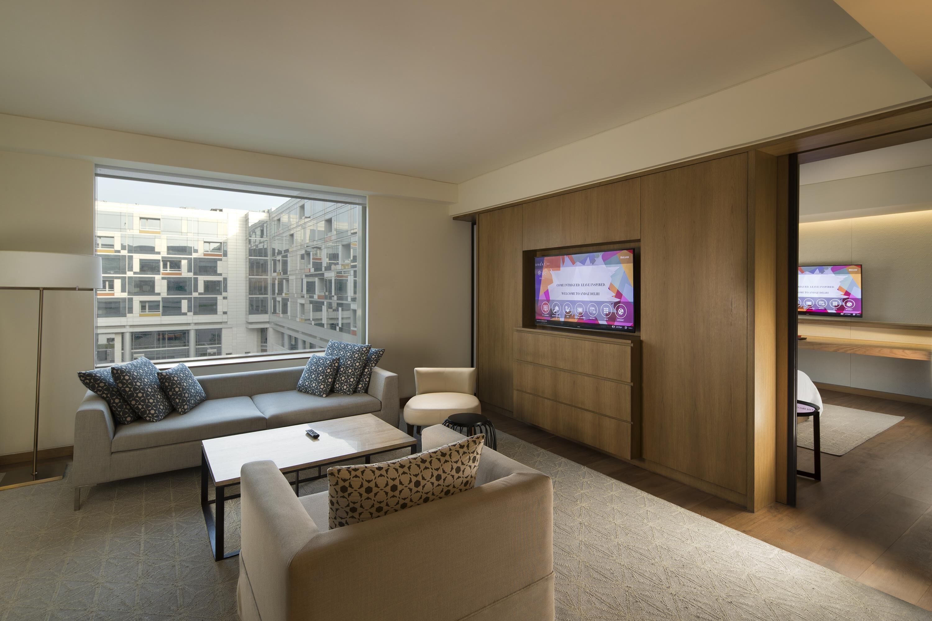 Une chambre d’hôtel moderne équipée d’un canapé, d’un fauteuil et d’un téléviseur fixé au mur.