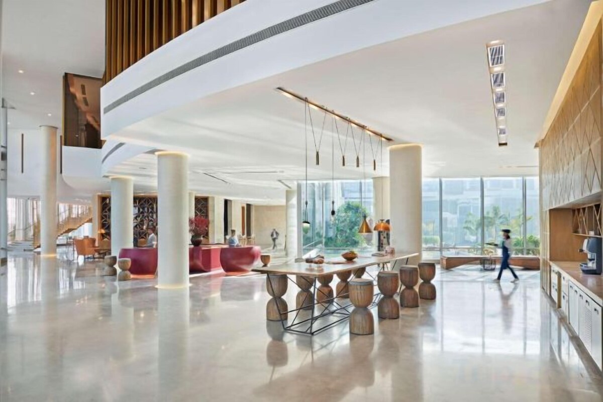 A spacious lobby with a central table, seating areas, and large windows offering a view of the outdoors.