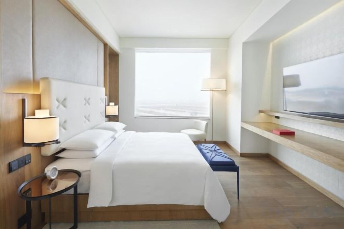 A hotel room with a bed, bedside tables, a window, and a television.