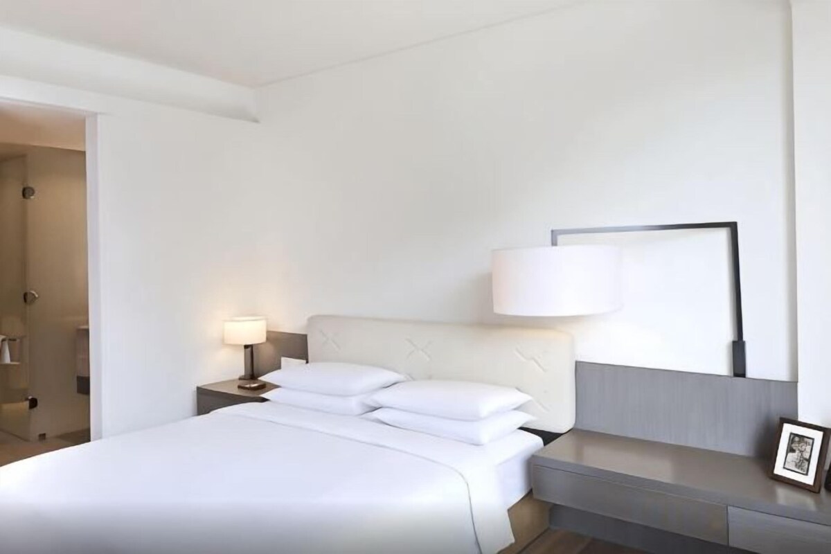 A hotel room with a bed, bedside table, lamp, and a framed picture.