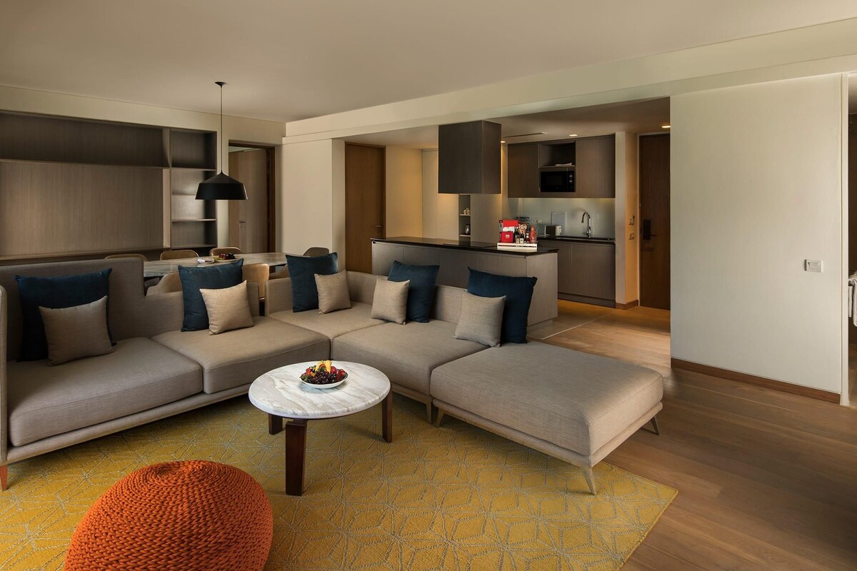 A modern living room with a sectional sofa, a round coffee table, and a small orange ottoman.