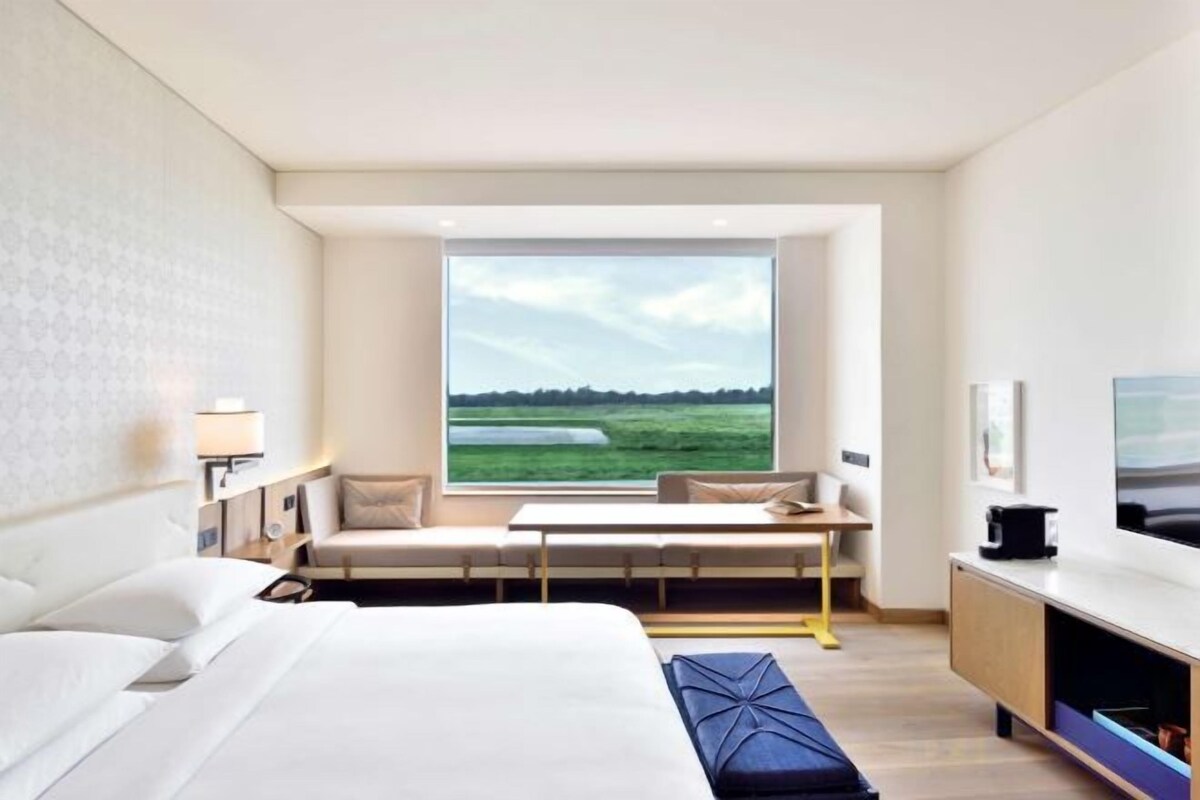 A hotel room with a large bed, a seating area with a view, a TV, and a desk.