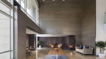 A spacious lobby with a high ceiling, a central wooden table, seating areas, and large windows allowing natural light.