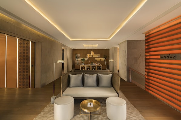 Un moderno vestíbulo de hotel con sofá, pufs, mostrador de recepción y una pared con placa.