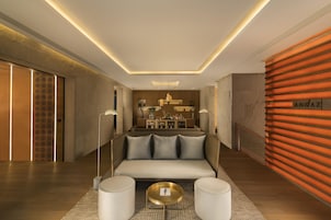 Un hall d’hôtel moderne avec un canapé, des poufs, un comptoir d’accueil et un mur orné d’une plaque signalétique.