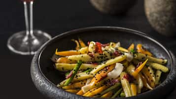 Un bol de salade de légumes colorée, parsemée de graines de sésame, accompagné d’un verre de vin rouge et d’un bol foncé.