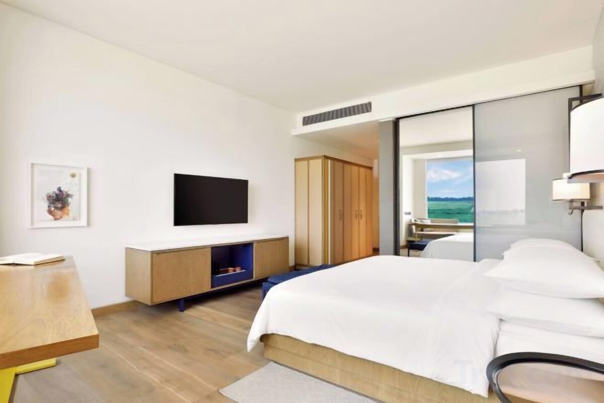 A hotel room with a bed, a TV on the wall, a wardrobe, and a view of the sea.