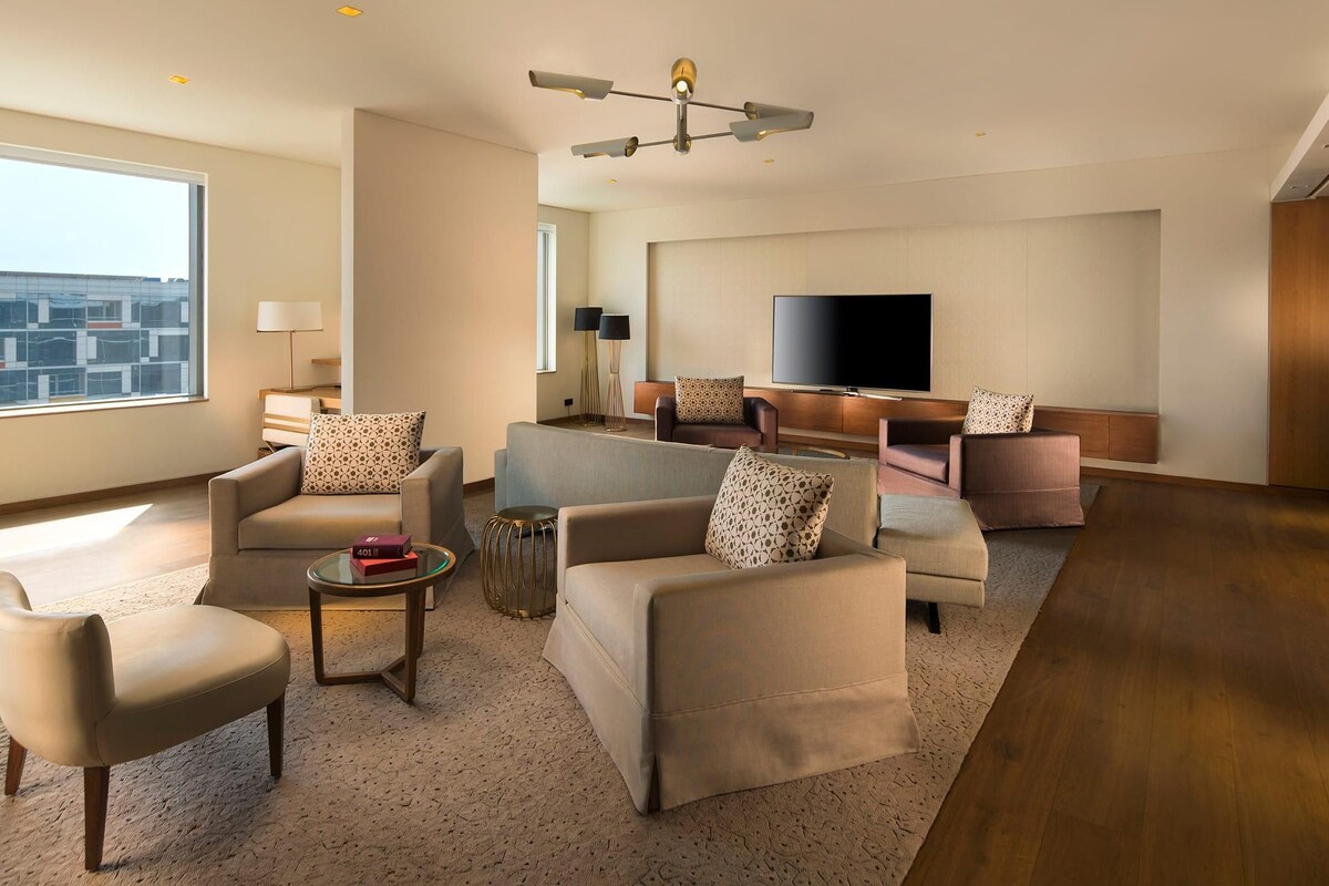 A modern living room with a large window, a flat-screen TV, and a seating area with sofas and armchairs.