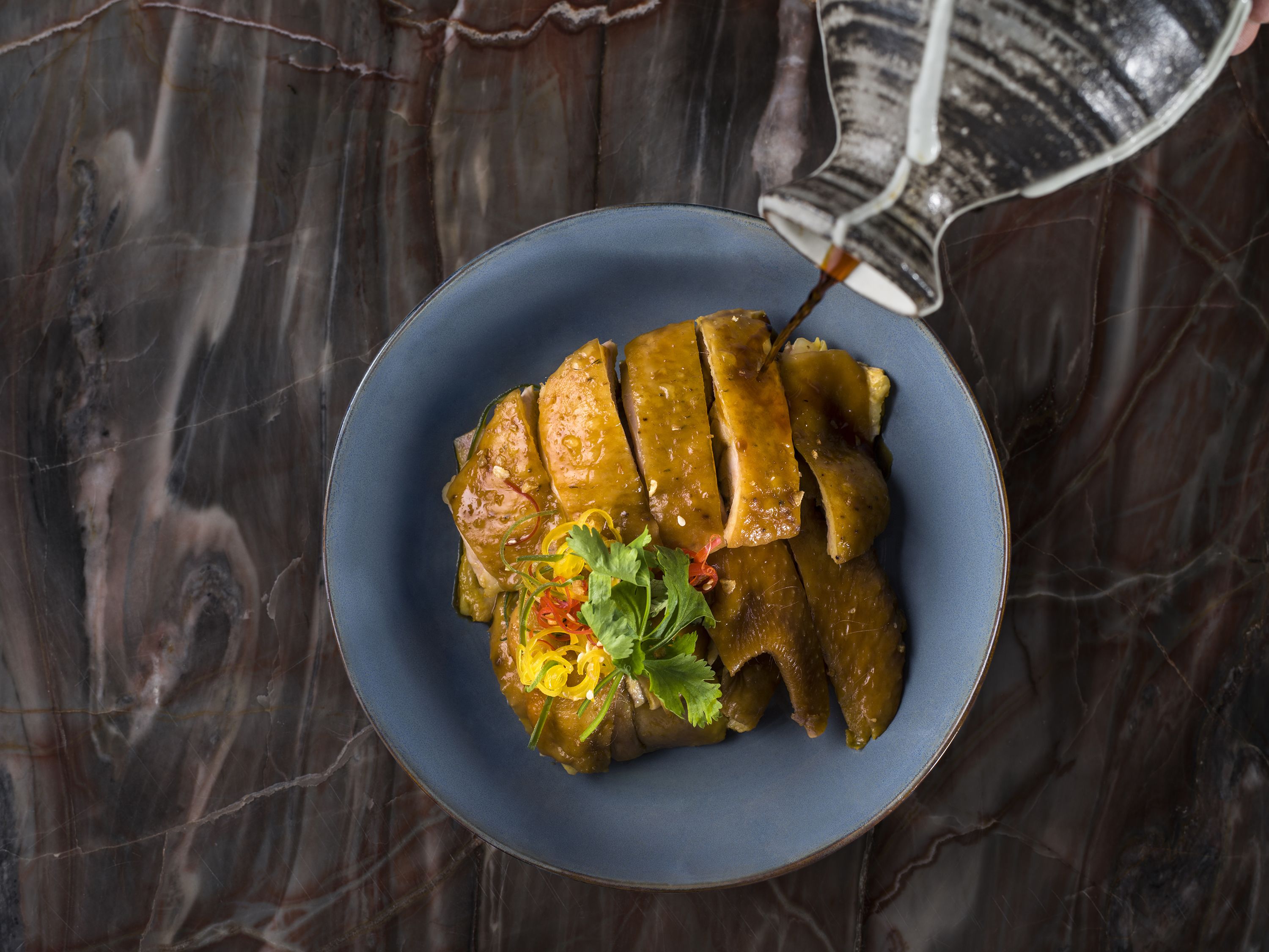 A plate of sliced duck with a sauce and garnishes on a dark marble surface.