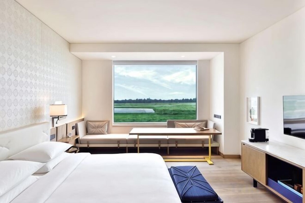 A modern hotel room with a large bed, a seating area with a view, a TV, and a desk.