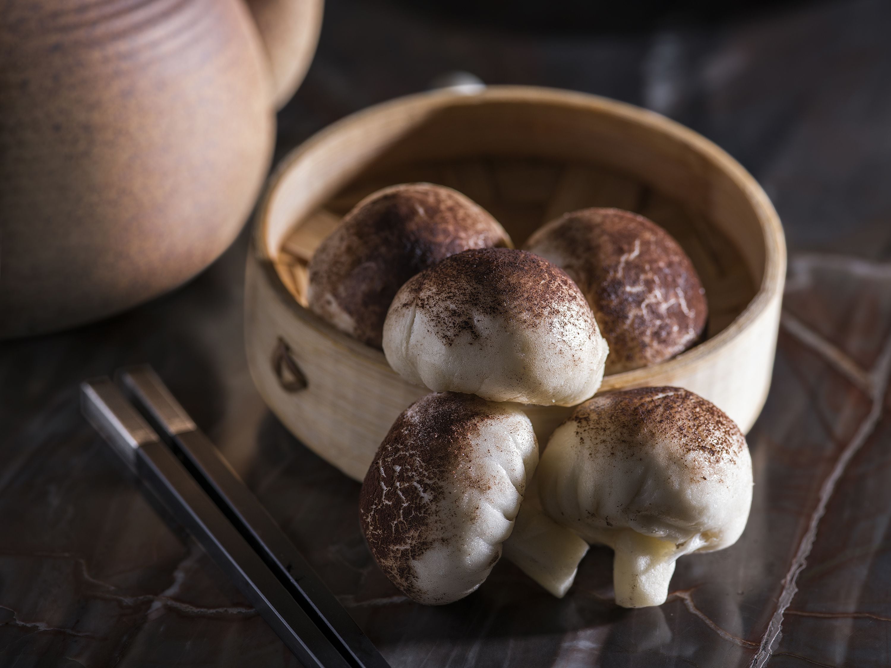 Un bol en bois contenant plusieurs petits pains, saupoudrés d’épices, posé sur un tissu sombre.