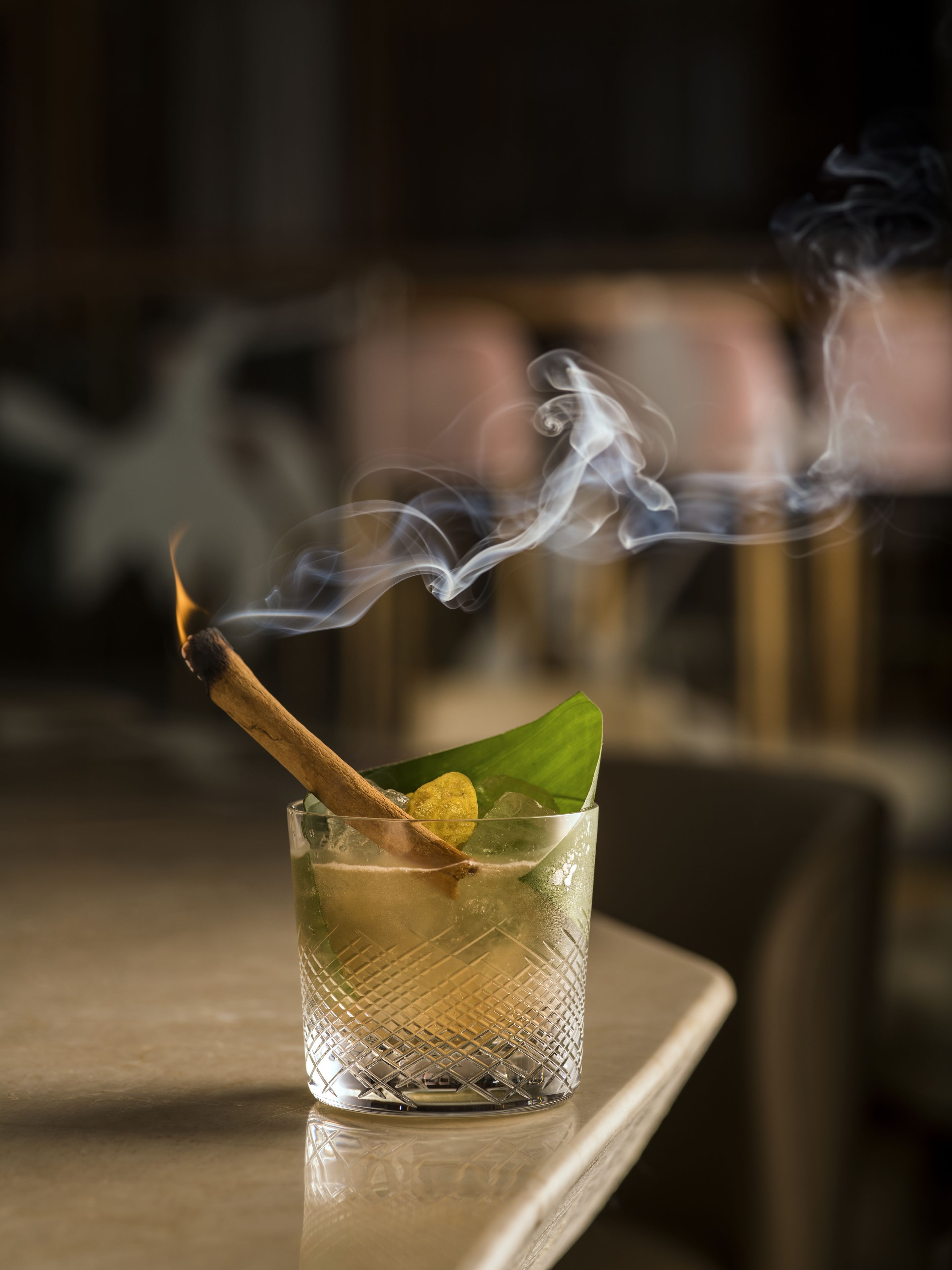 A glass with a wooden stick and a green leaf on a reflective surface.