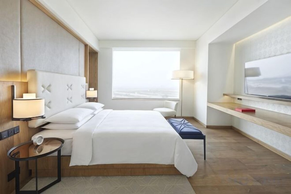 A hotel room with a large bed, bedside tables, a window with a view, and a TV on the wall.