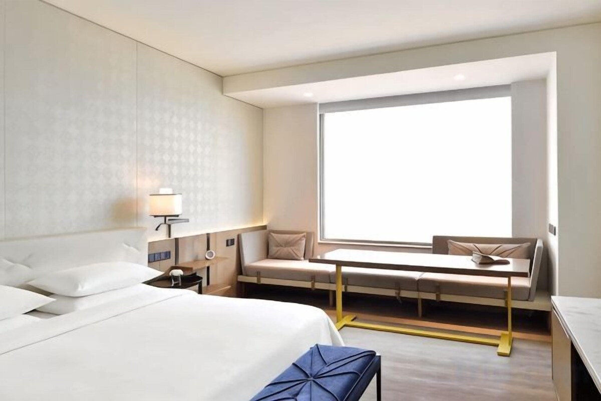 A hotel room with a large bed, a seating area with a table, and a window providing natural light.