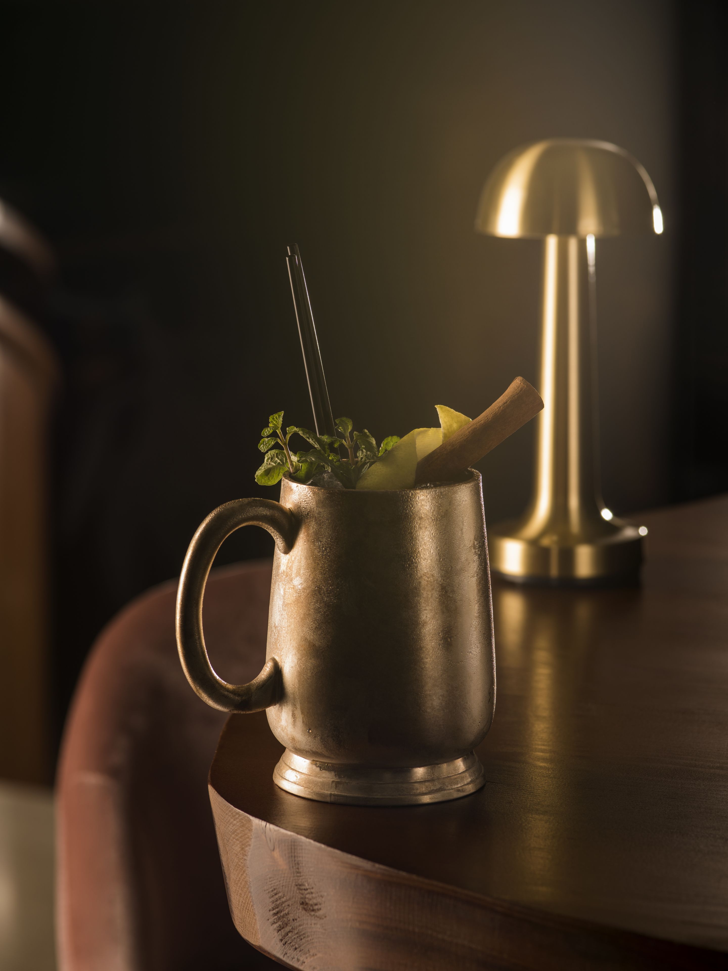 A metallic mug with a spoon and a plant on a wooden surface.