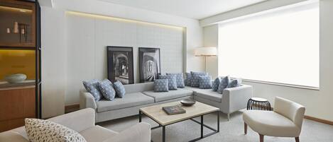 A modern living room with a grey sofa set, patterned cushions, a coffee table, and a large window providing natural light.