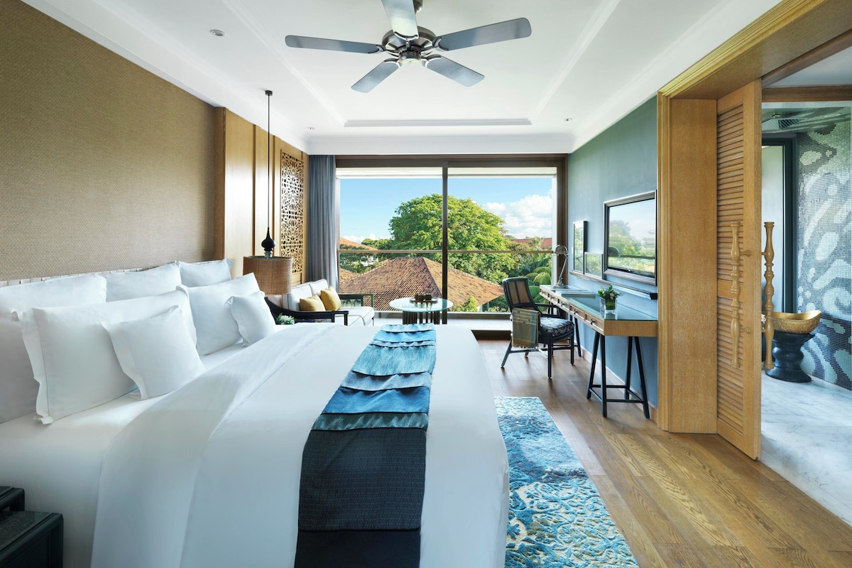 A hotel room with a large bed, a desk, a chair, a ceiling fan, and a view of the outdoors.