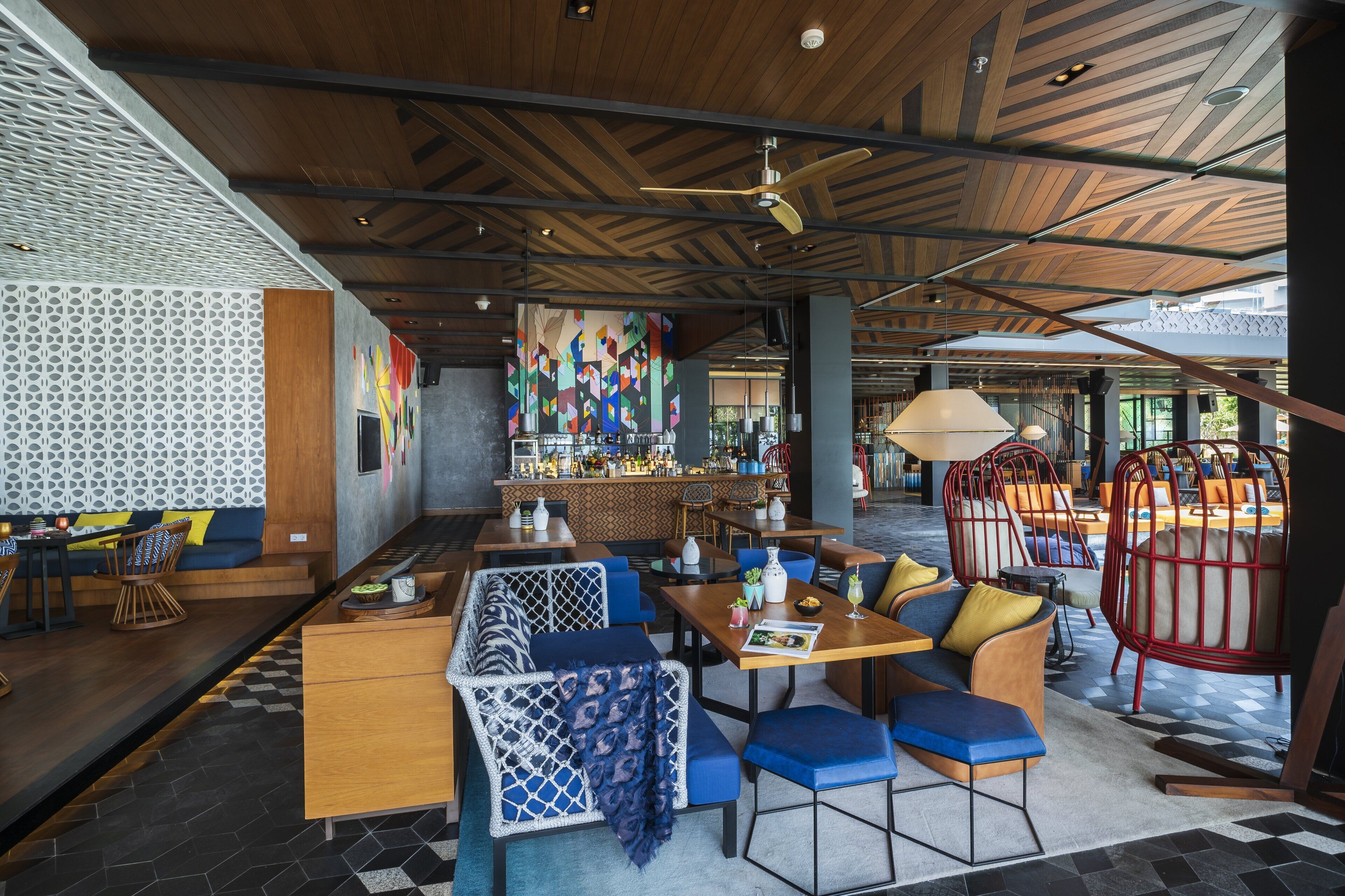 A modern restaurant with a bar area, seating arrangements, and a patterned ceiling.