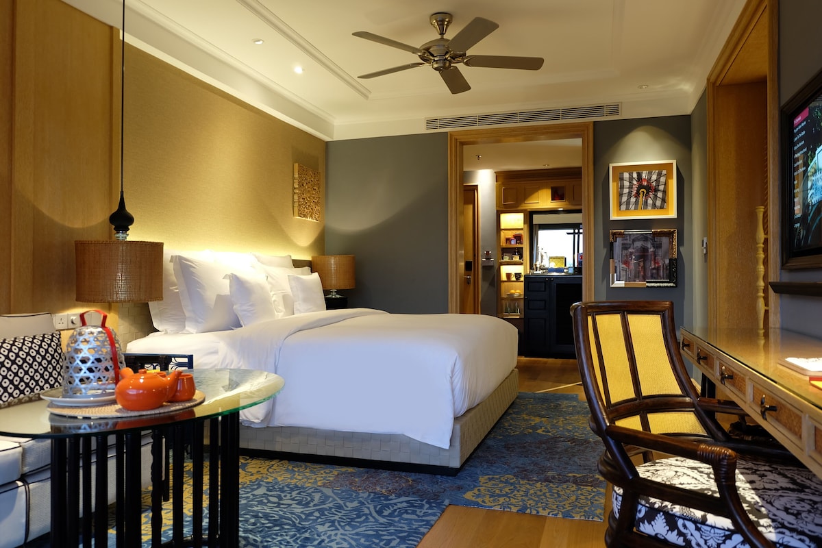 A hotel room with a bed, a chair, a table with a lamp, and a television.
