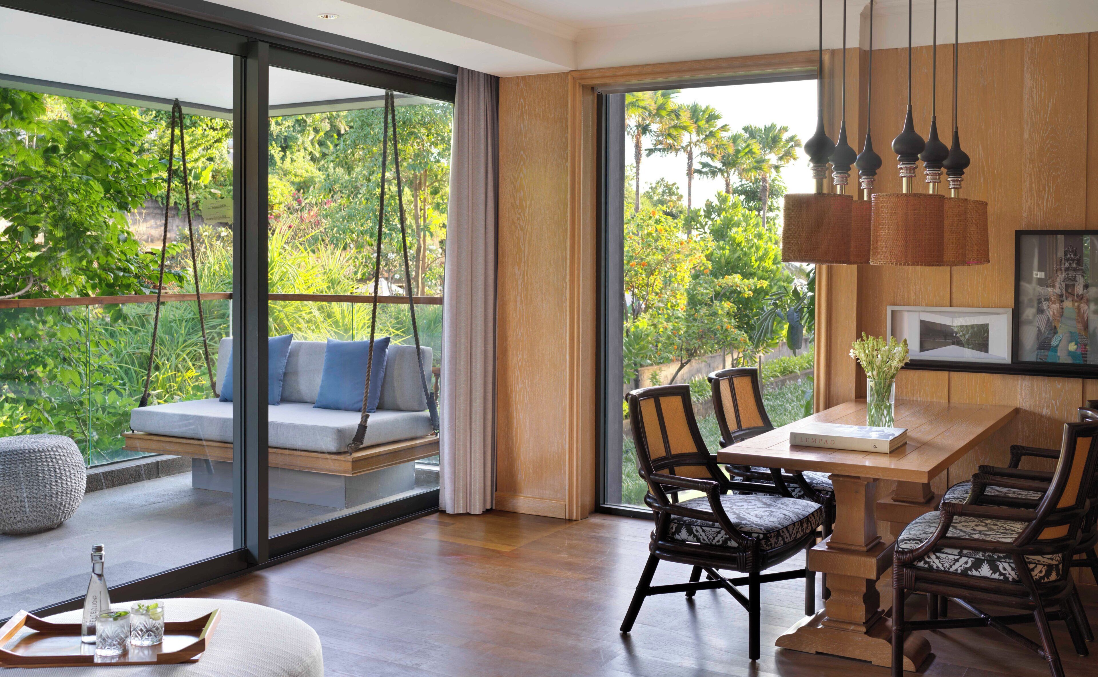 A modern interior with a dining area, a swing seat by a large window, and a view of greenery outside.