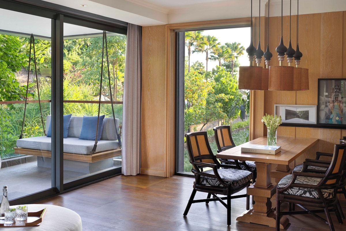 A modern interior with a dining area, a sofa with cushions, and a view of lush greenery outside.