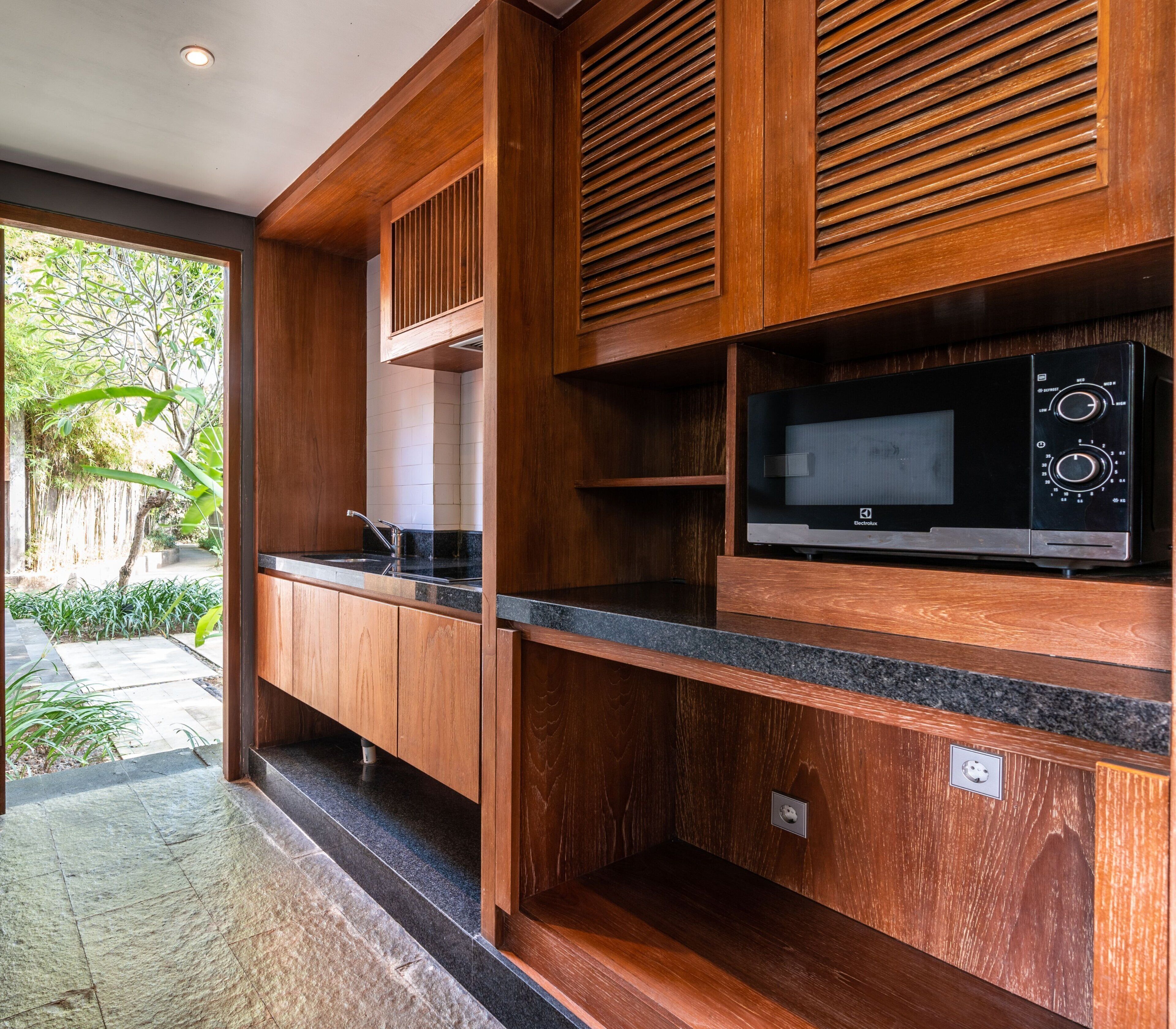 A modern kitchen with wooden cabinetry, a built-in microwave, and a view of the outdoor garden.