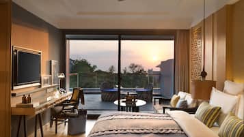 Quarto moderno com cama grande, escrivaninha, cadeira e varanda com vista para o pôr do sol.