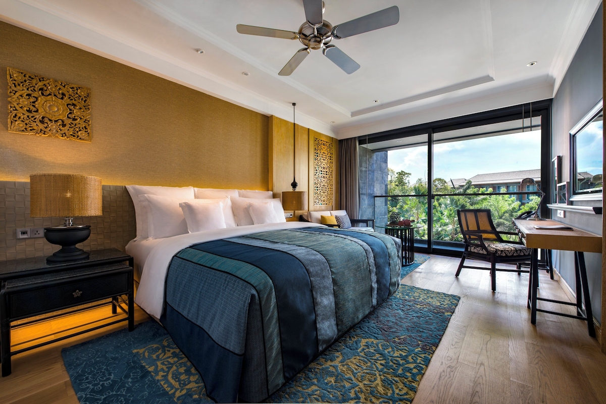 A modern bedroom with a large bed, a desk, and a view of the outdoors.