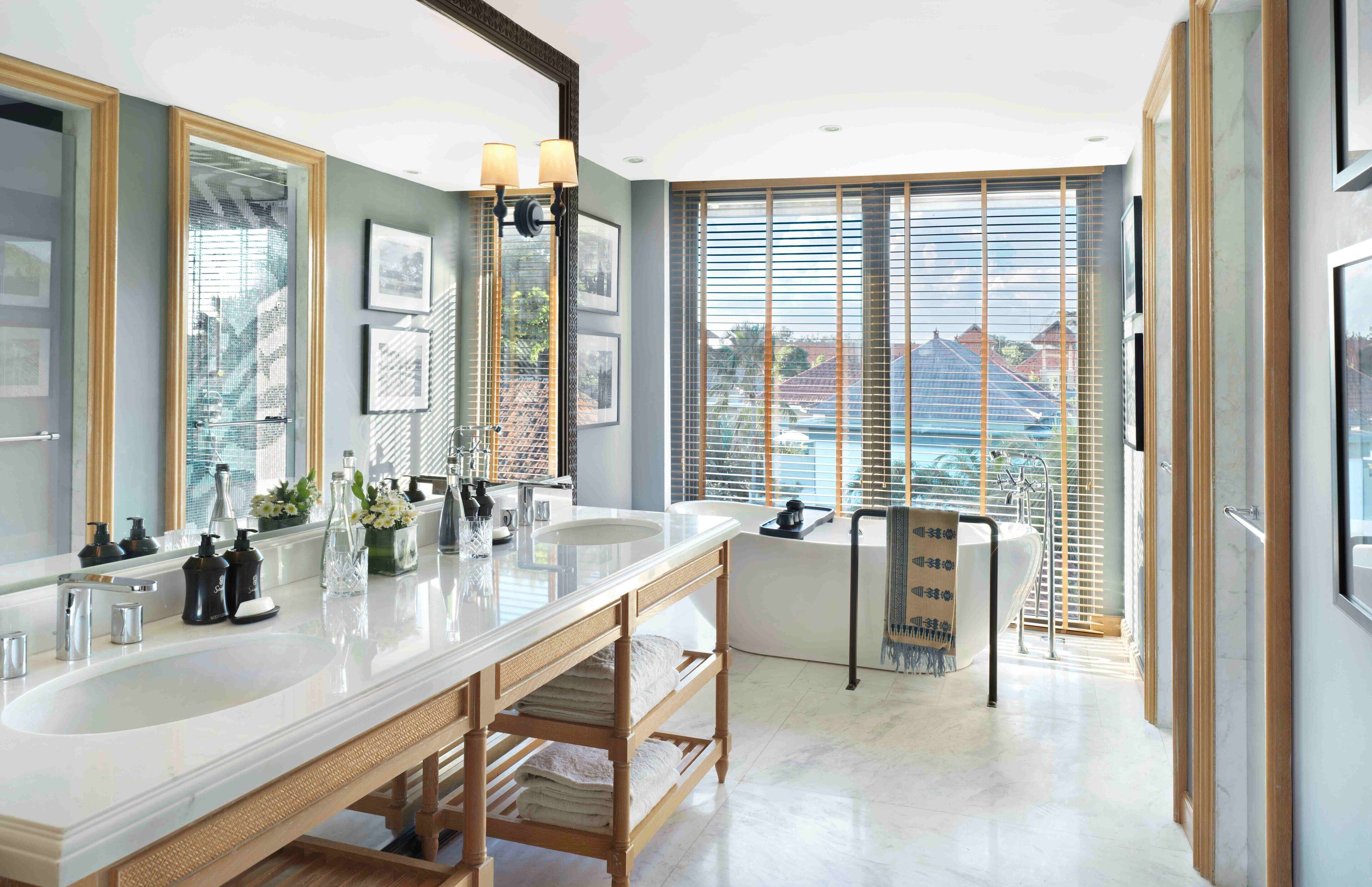 A modern bathroom with a large mirror, two sinks, and a bathtub.