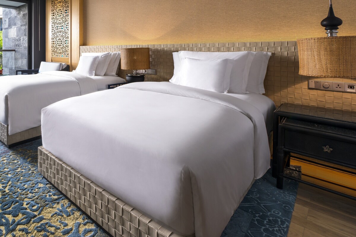 A hotel room with two beds, a nightstand, a lamp, and a decorative wall panel.