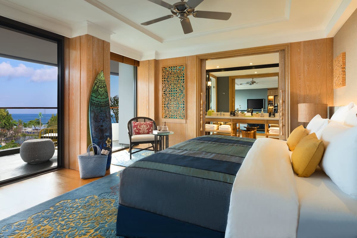 Ein modernes Hotelzimmer mit einem großen Bett, einem Balkon mit Blick und einem Deckenventilator, sowie einem Badezimmer mit großem Spiegel.