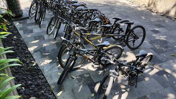 Uma fileira de bicicletas estacionadas em superfície pavimentada, com uma moldura de pedra e vegetação ao lado.