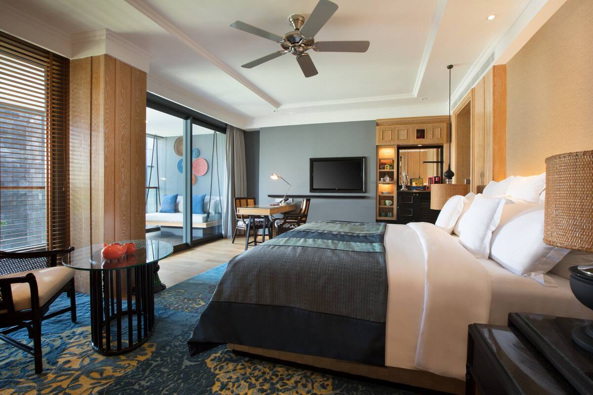 Ein Hotelzimmer mit Bett, Schreibtisch, Stuhl, Fernseher und Deckenventilator.