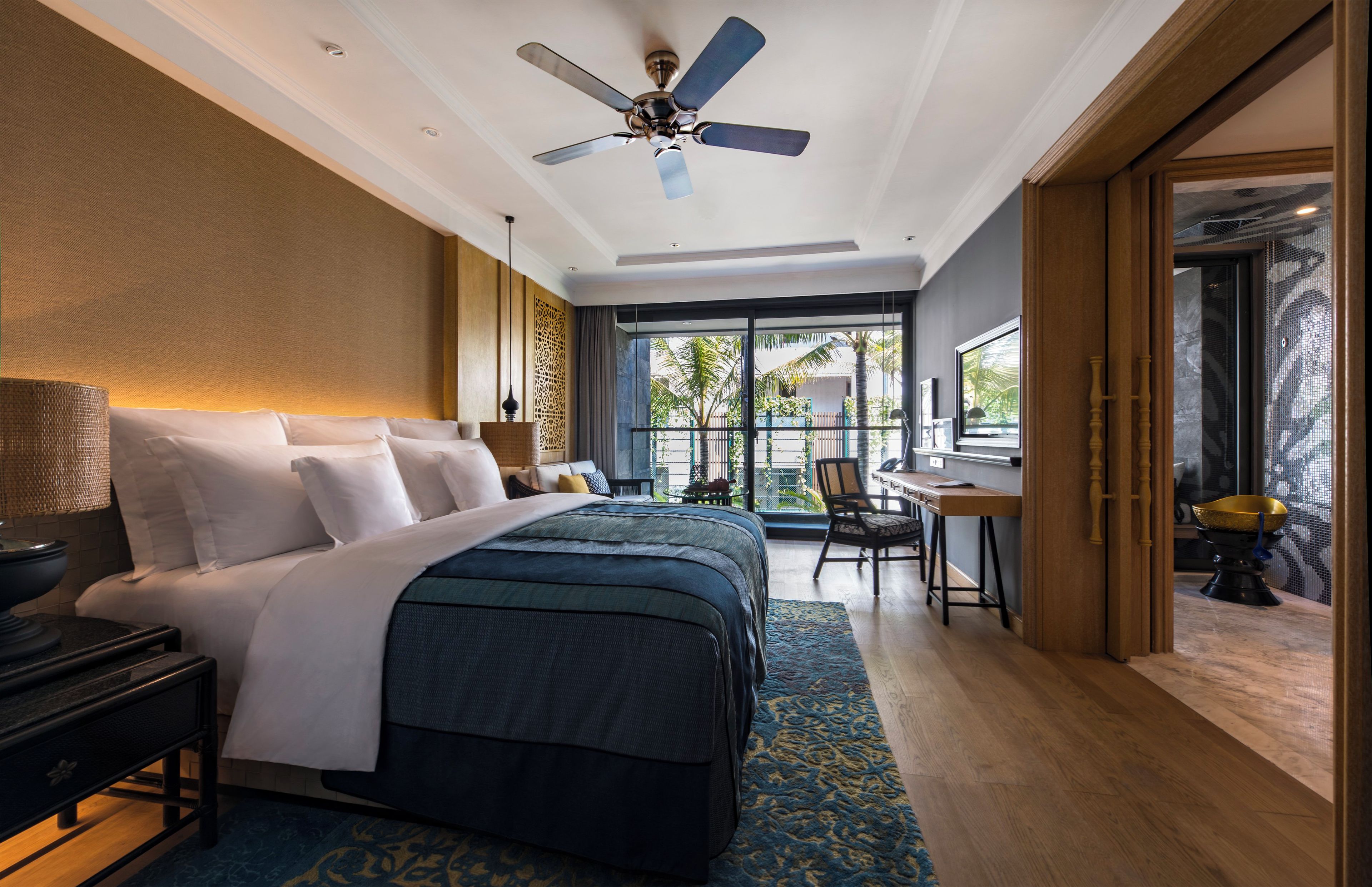 A hotel room with a bed, desk, chair, and a view of the outdoors.