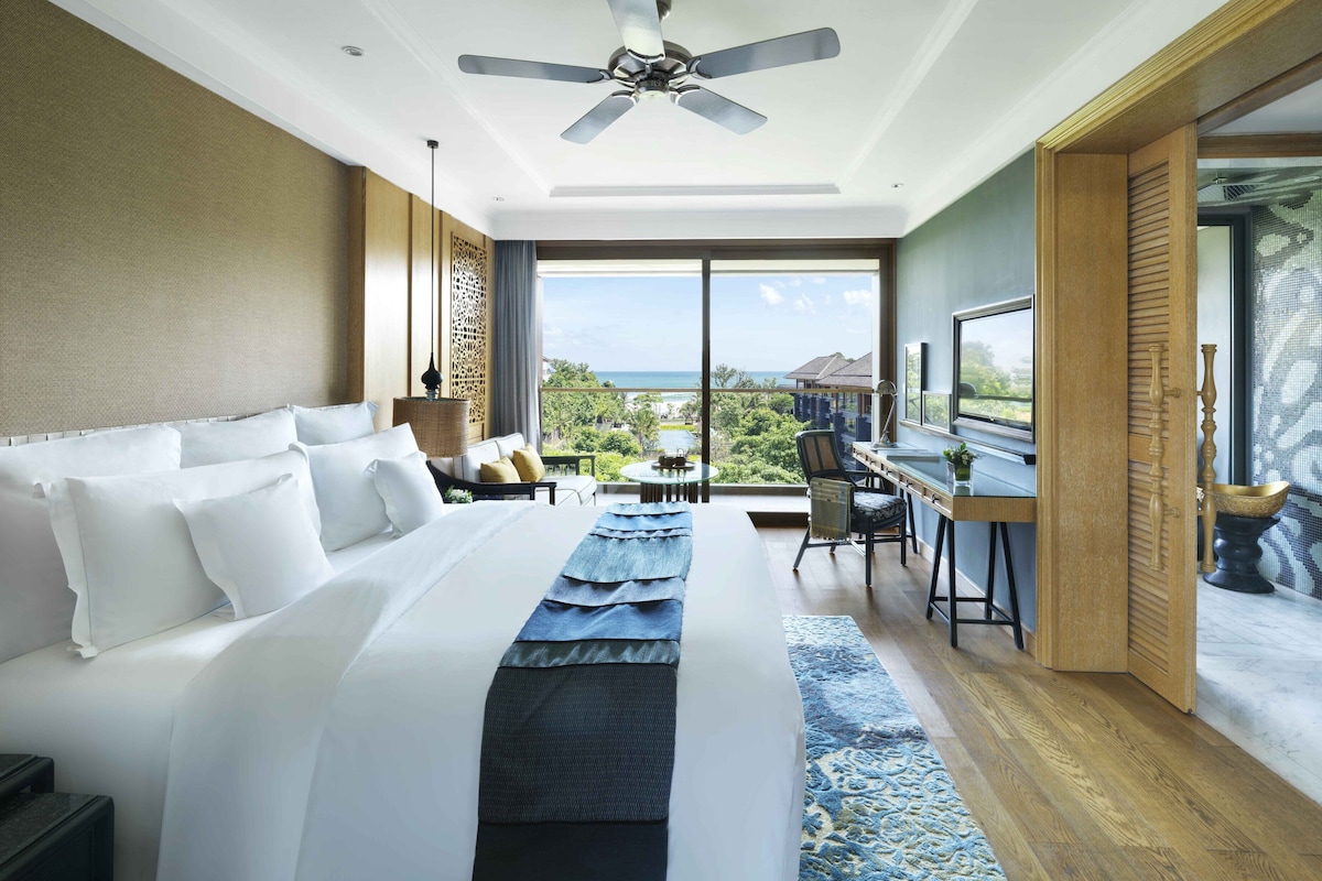 A hotel room with a large bed, a desk, and a view of the ocean.
